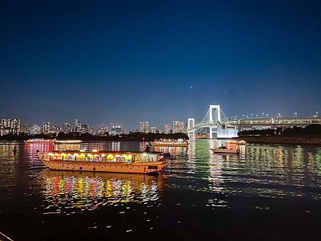 Una Yakatabune a Tokyo naviga nella baia di notte con il Rainbow Bridge illuminato sullo sfondo.