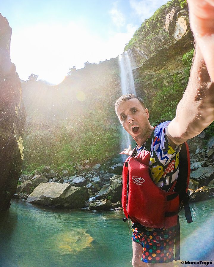 Marco Togni davanti alle Cascate di Pinaisara con giubbotto rosso