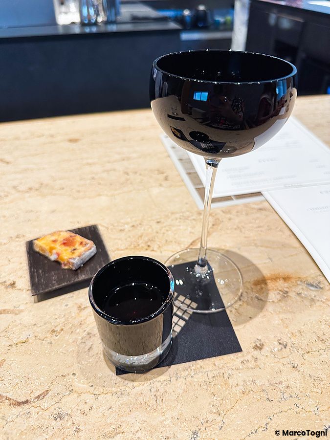 Un assaggio di caffè a Koffee Mameya Kakeru con un calice, una tazzina nera e un dolcetto su un bancone in pietra.