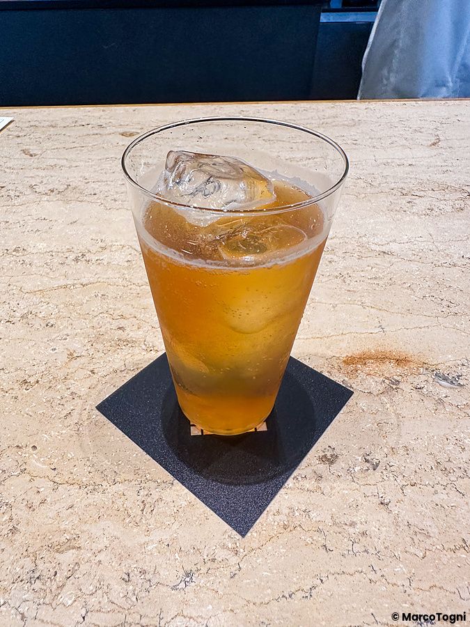 Un cocktail con caffè servito con ghiaccio in un bicchiere trasparente su un sottobicchiere nero da Koffee Mameya Kakeru.