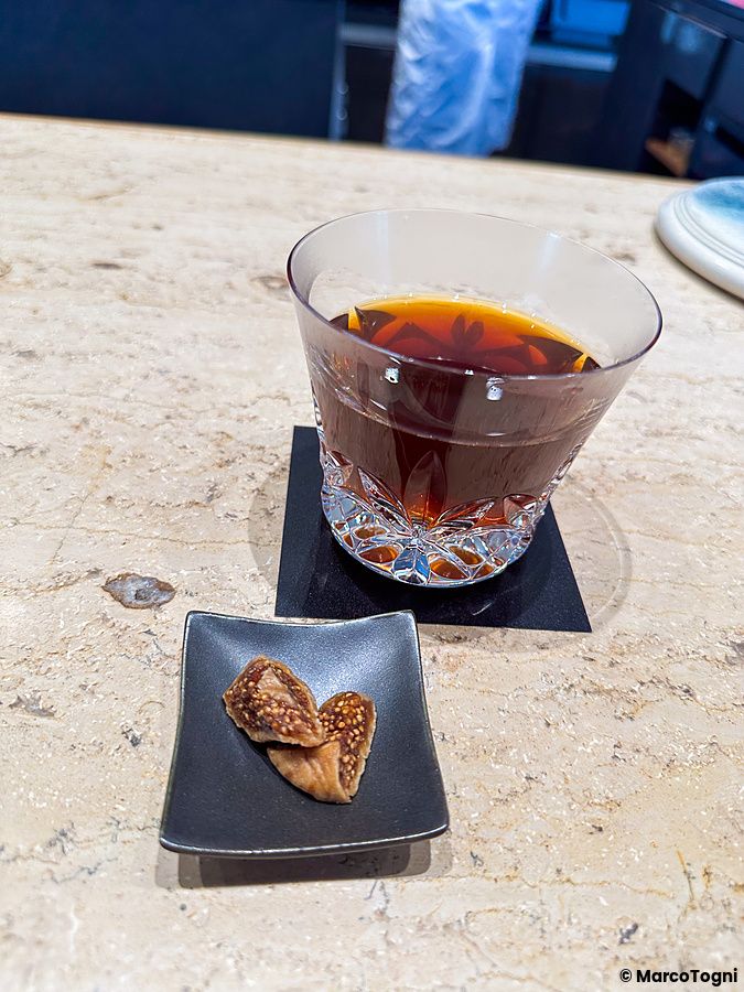 Un assaggio di caffè a Koffee Mameya Kakeru con un bicchiere di caffè nero e fichi essiccati su un bancone di pietra.