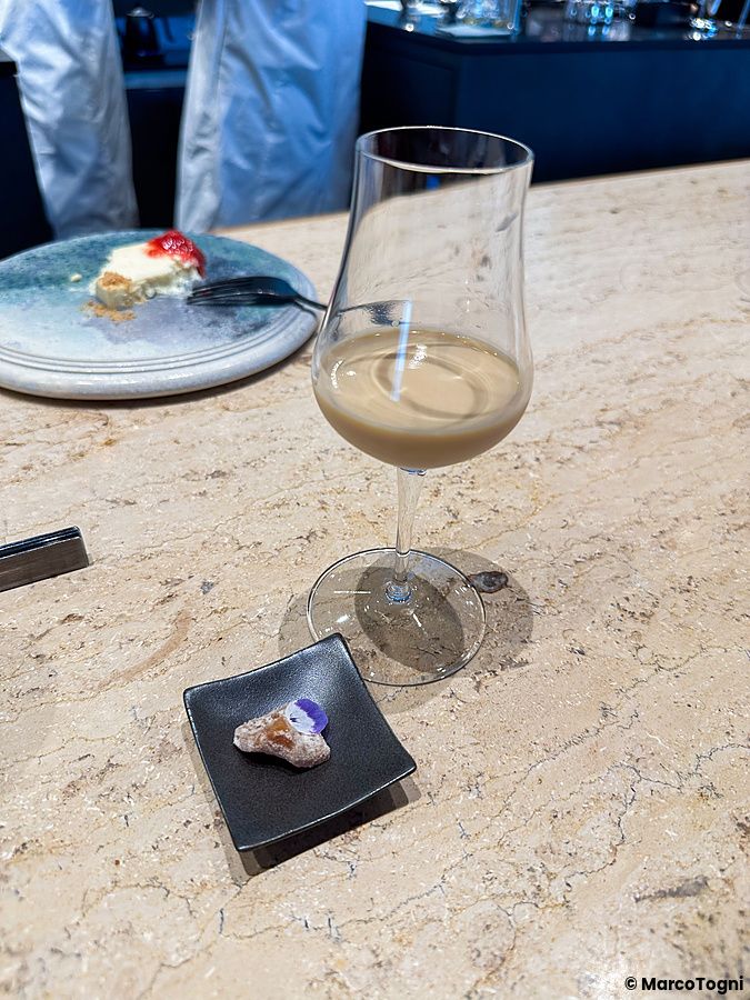 Un assaggio di caffè a Koffee Mameya Kakeru con un calice di bevanda e un piccolo dolcetto su un bancone di pietra.