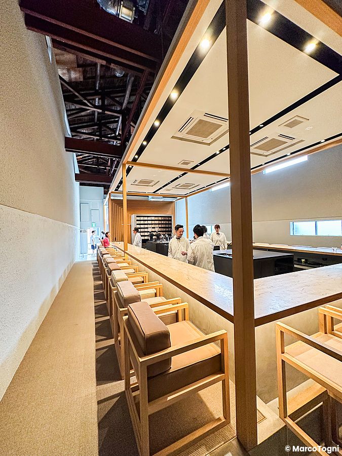 Interno del locale Koffee Mameya Kakeru a Tokyo con un lungo bancone in legno e persone che servono il caffè.