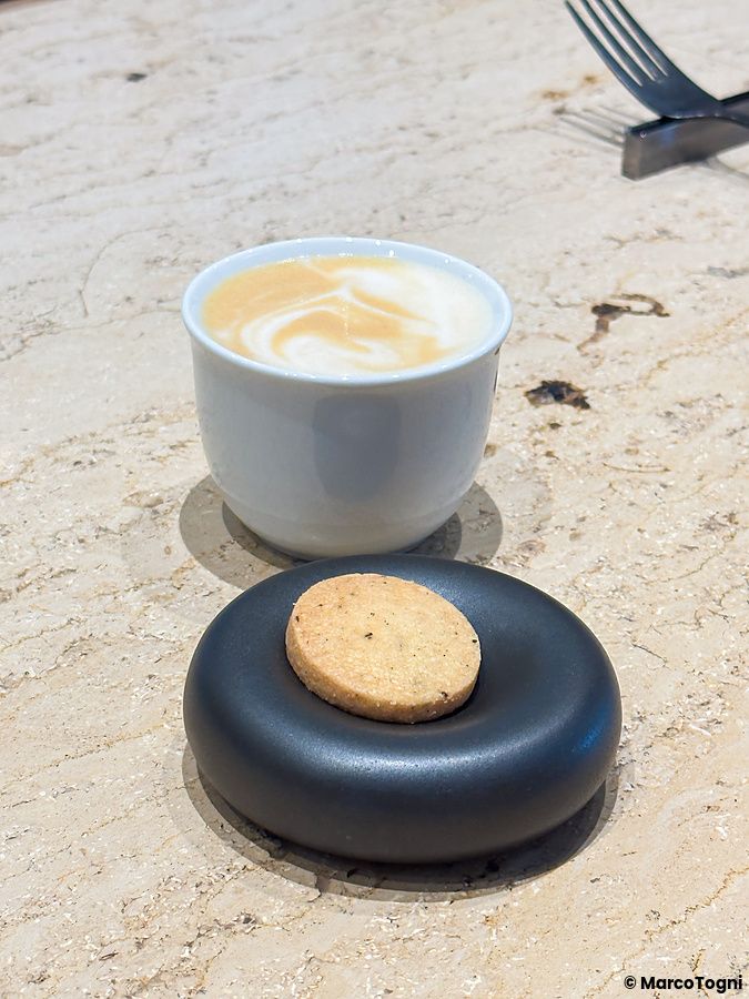 Tazzina di caffè con latte e un biscotto su un supporto nero presso Koffee Mameya Kakeru a Tokyo.