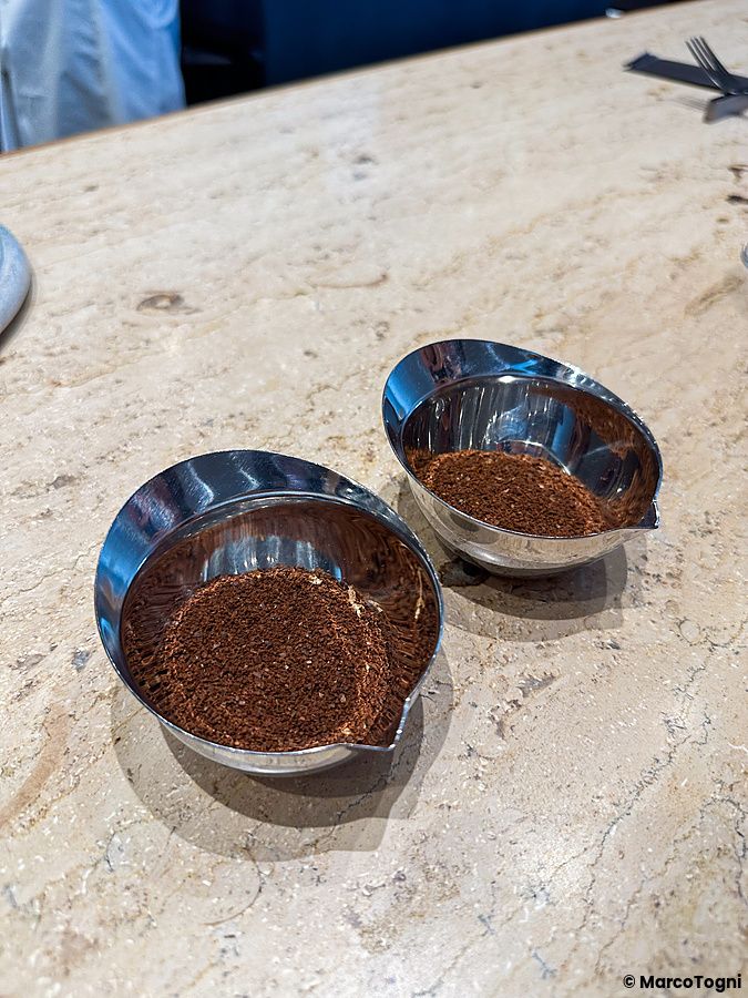 Due ciotole in metallo contenenti polvere di caffè a Koffee Mameya Kakeru appoggiate su un piano in pietra.