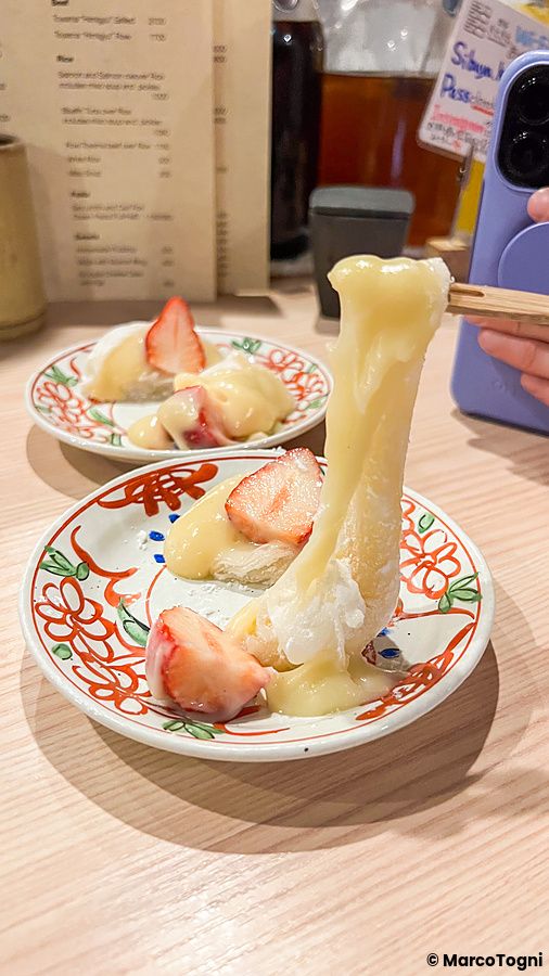 Un daifuku con fragole e crema sollevato da bacchette su un piattino decorato presso lo Shibuya Kito Kito a Shibuya.