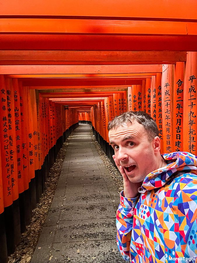 Marco Togni in giacca colorata tra i torii di Fushimi Inari a Kyoto.