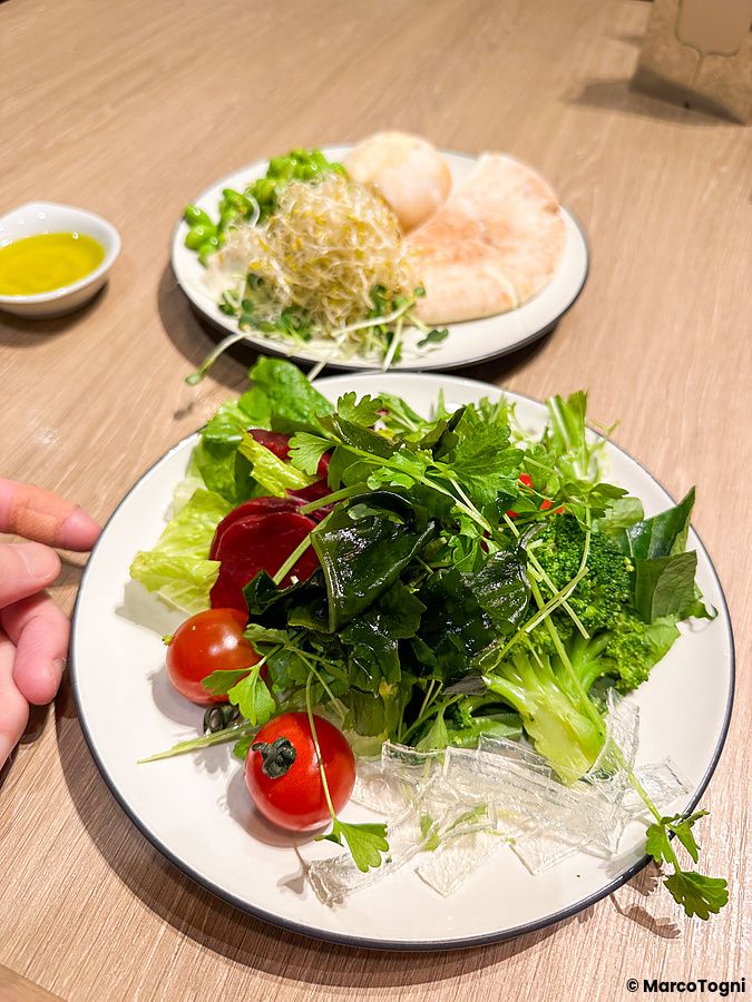 Due piatti con insalata mista e pane pita su un tavolo in legno all'interno di un ristorante Sizzler.
