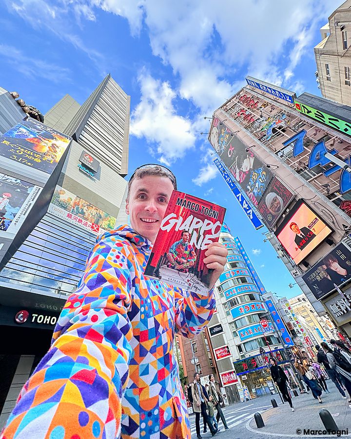 Marco Togni in giacca colorata con libro "Giappone" nelle strade di Kabukicho, Tokyo.