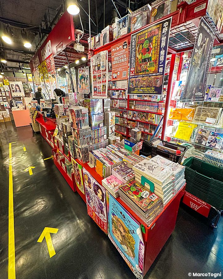 Interno del negozio Mandarake a Nakano, Tokyo, con scaffali carichi di manga e una persona alla cassa.