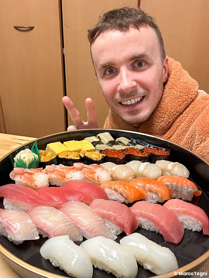 Marco Togni sorridente con un vassoio di sushi in Giappone.