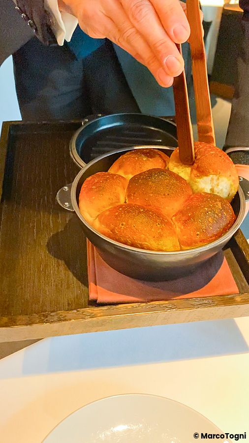 Una persona serve pane artigianale a L'Effervescense utilizzando una pinza di legno all'interno di una pentola scura.