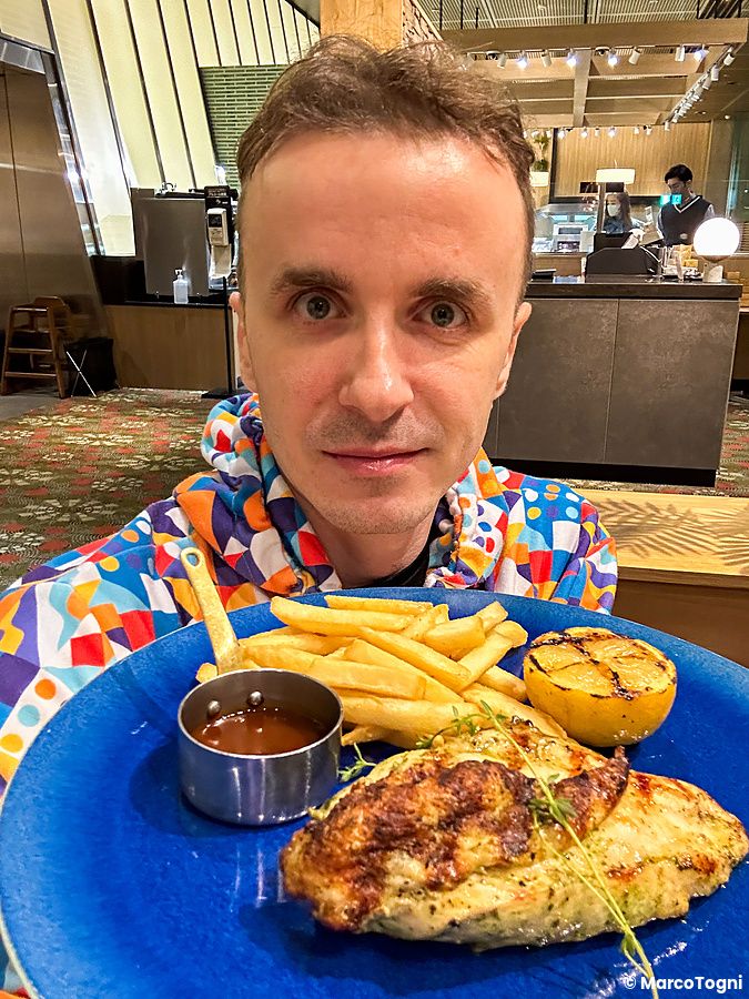 Marco Togni tiene in mano un piatto blu con pollo a Sizzler, patatine, salsa e limone all'interno del ristorante.