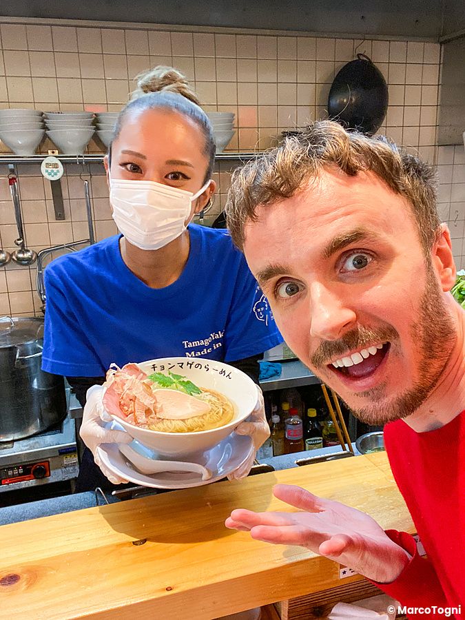 Marco Togni sorridente si scatta un selfie con una dipendente del Ramen Chonmage Osaka Tenroku Ten che porge una ciotola.