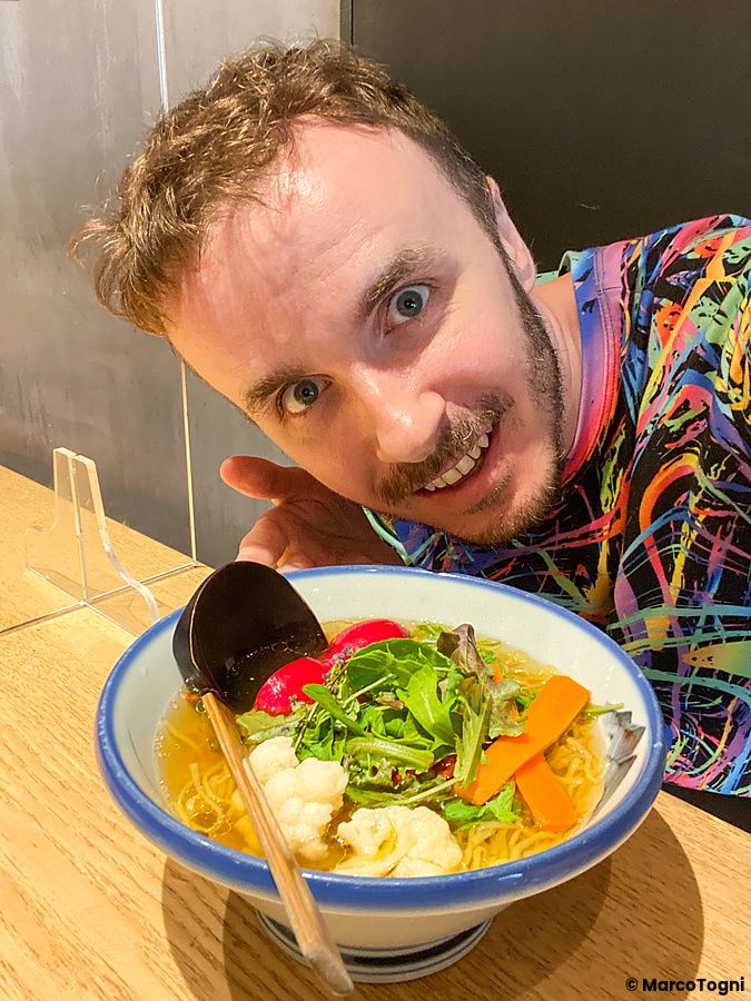 Marco Togni sorride vicino a una ciotola di ramen vegano servita nel ristorante Afuri in Giappone.