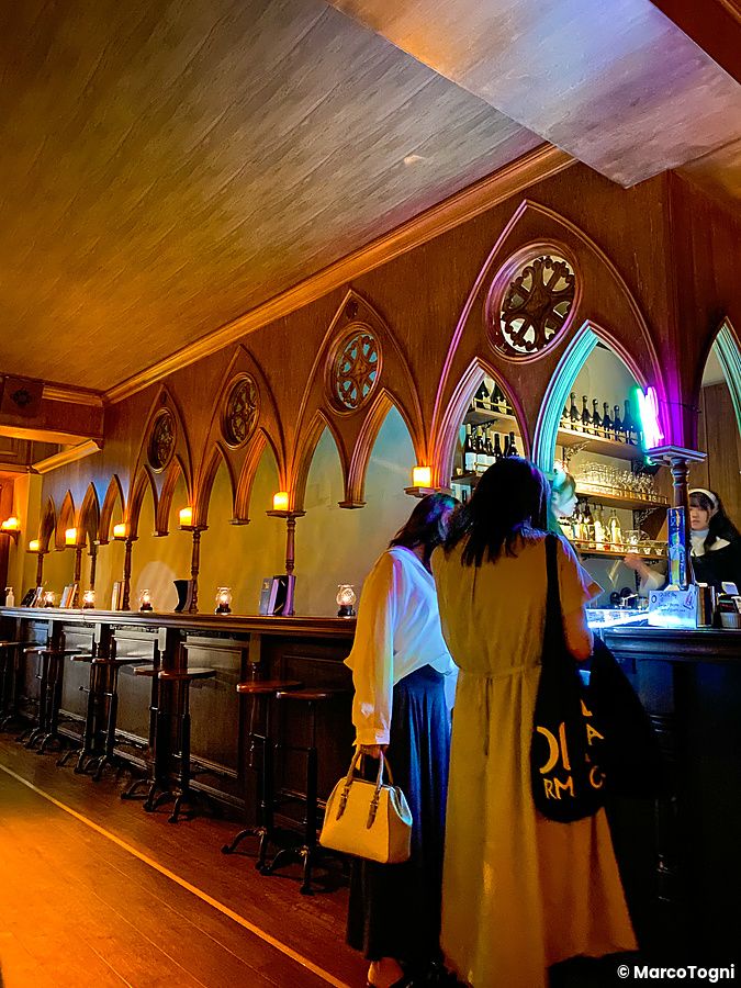 Interno del bar a tema The Church a Shibuya, con archi neogotici, bancone e persone che consumano bevande.