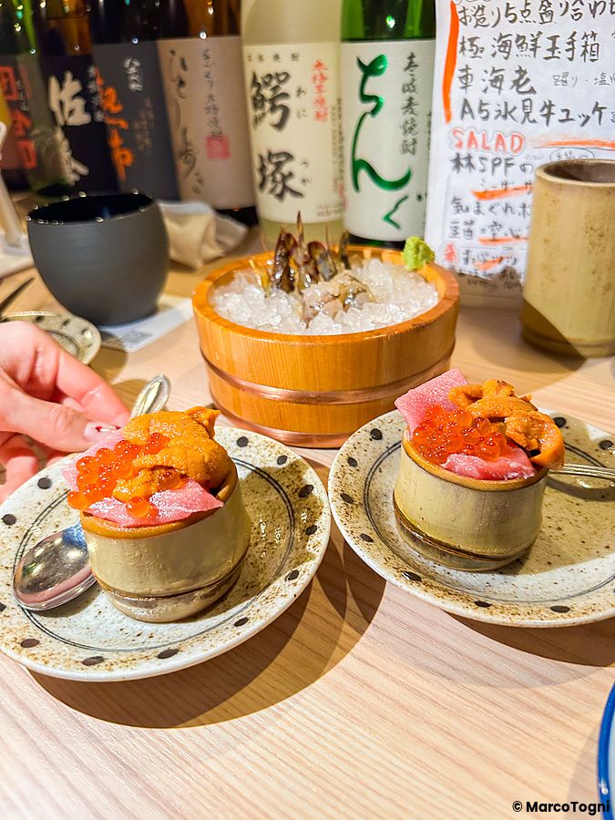Piattini con crudo di mare serviti in un izakaya a Shibuya Kito Kito con bottiglie di sake sullo sfondo.