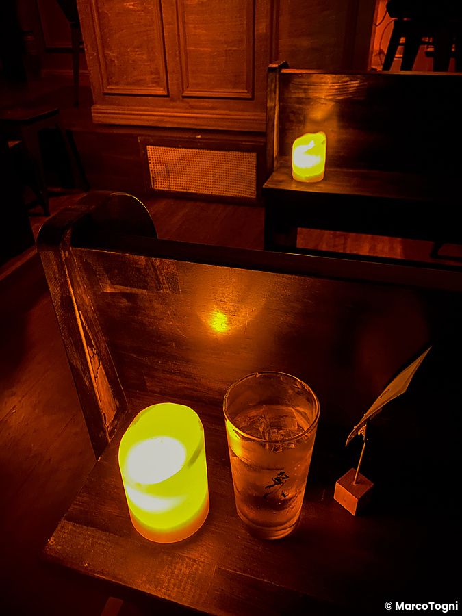 Un cocktail e una candela illuminata su una panca in legno all'interno del bar a tema The Church a Shibuya.