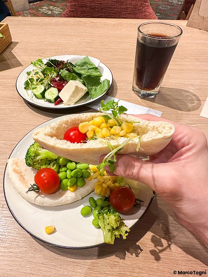 Una mano sostiene una pita con mais e verdure accanto a un piatto di insalata in un ristorante Sizzler.