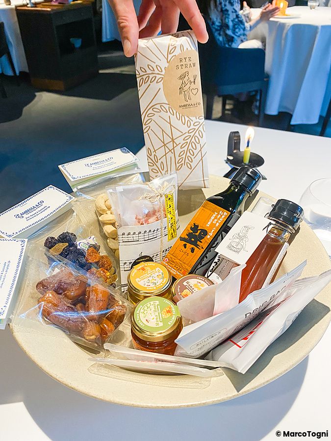 Una mano tiene una confezione di cannucce sopra un piatto pieno di vari prodotti alimentari souvenir a L'Effervescense.