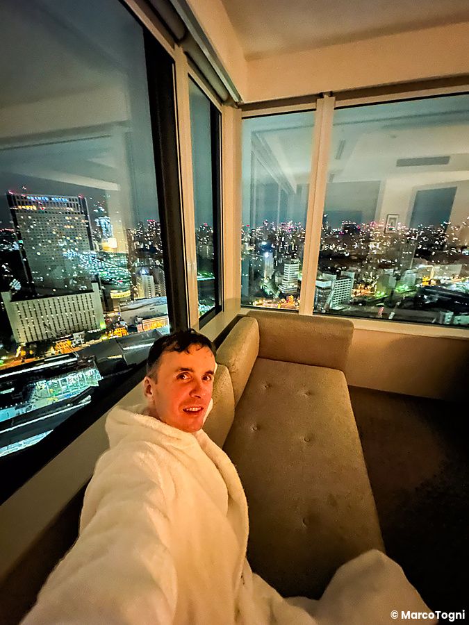 Marco Togni in accappatoio si rilassa su un divano in una stanza dell'InterContinental the Strings Tokyo con vista città.