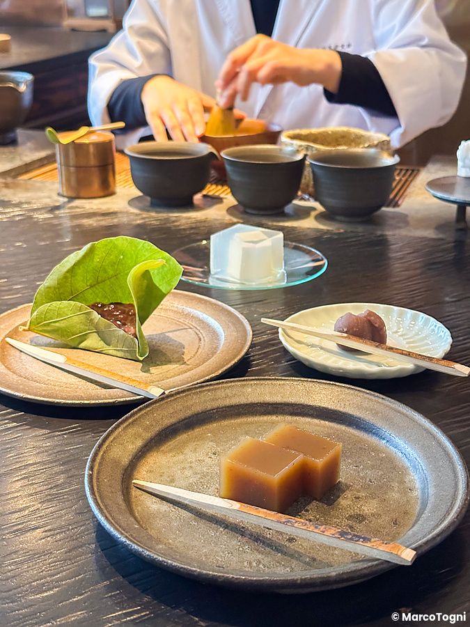 Un tavolo con dolci tradizionali wagashi e una persona che prepara il tè presso Sakurai Japanese Tea Experience a Tokyo.