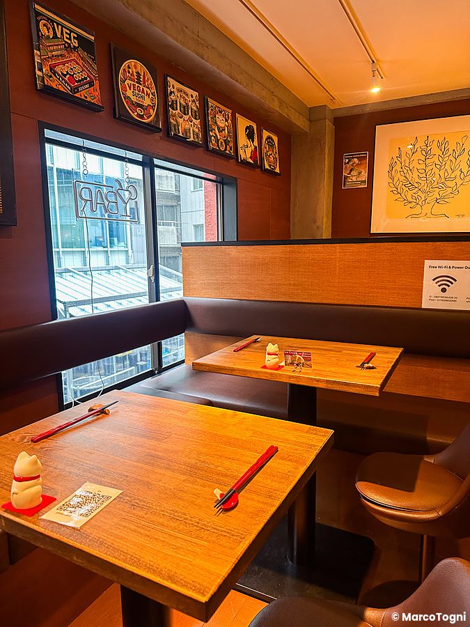 L'interno a Vegan Sushi Tokyo presenta tavoli in legno con bacchette rosse disposti vicino a una finestra.