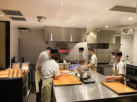 La cucina del ristorante Crony, Tokyo, con lo staff al lavoro attorno a banconi in acciaio.