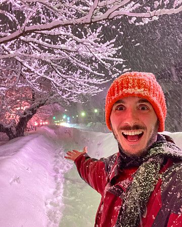 Marco Togni con cappello arancione sotto alberi di sakura innevati al parco di Hirosaki