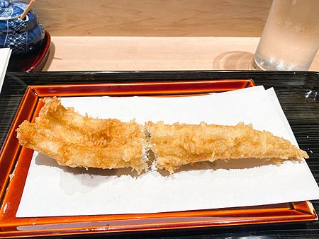 Un filetto di grongo in tempura adagiato su carta assorbente su un vassoio rettangolare al Tempura Kondo di Ginza.