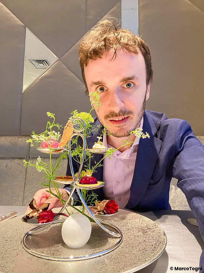 Marco Togni siede a un tavolo del ristorante Asahina Gastronome con un amuse-bouche di piccoli bocconcini decorati con aneto.