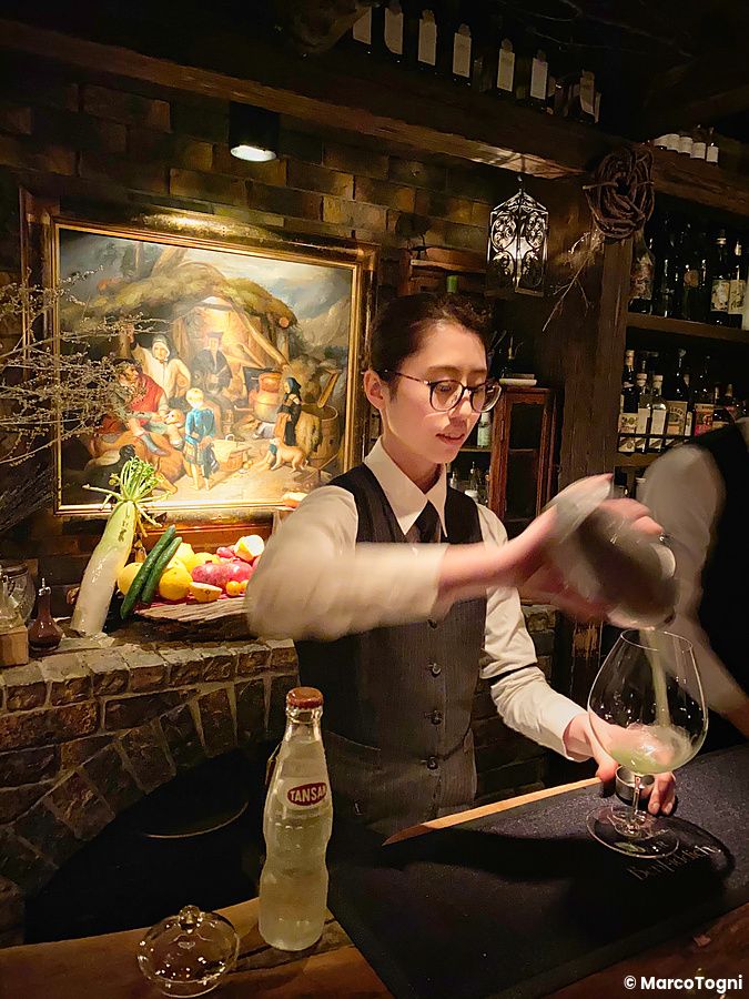Una donna aiutante barista prepara un drink dietro il bancone del Bar Benfiddich a Shinjuku.