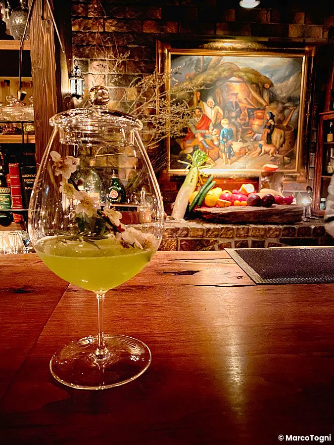 Un cocktail verde con decorazioni floreali sul bancone del Bar Benfiddich, dove lavora un aiutante barista.