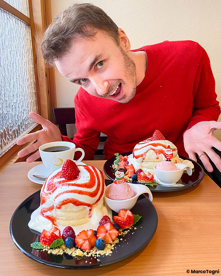Marco Togni sorridente dietro due piatti di pancake di Natale a Chaka decorati con fragole e crema.