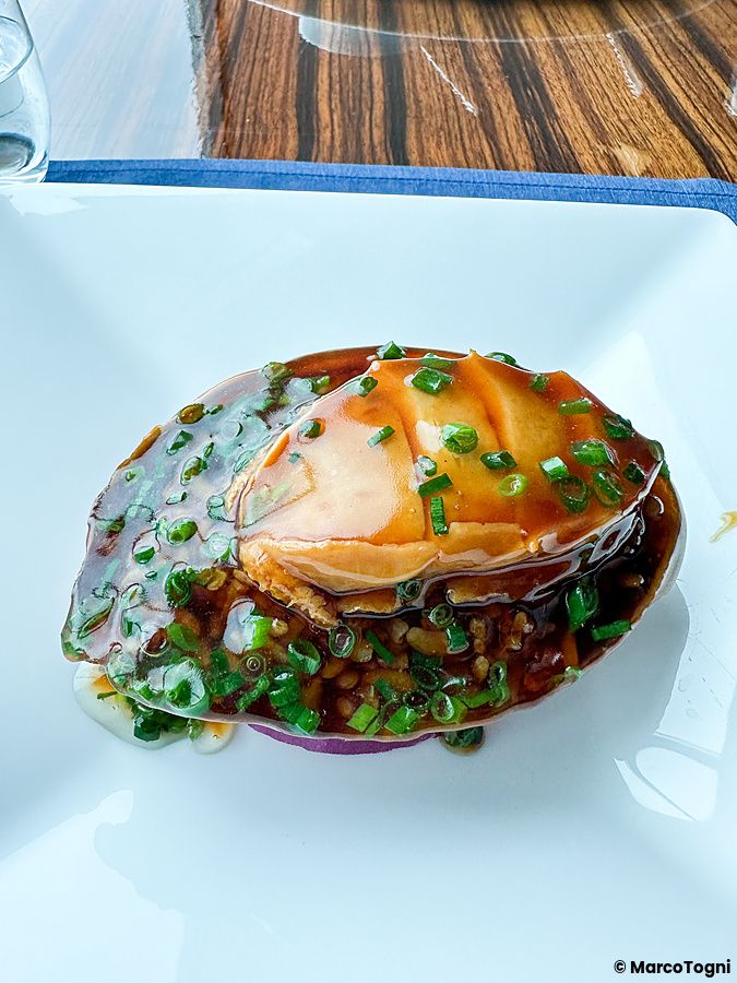 Abalone brasato con cipollotto servito in un piatto bianco al ristorante China Blue presso l'hotel Conrad a Tokyo.