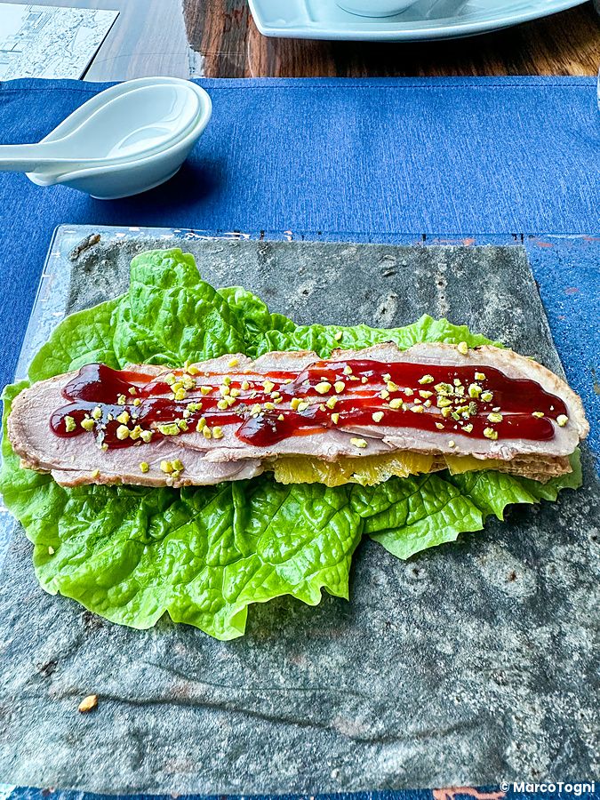 Anatra laccata a fette con salsa a China Blue a Tokyo servita su una foglia di lattuga e una base di pietra scura.