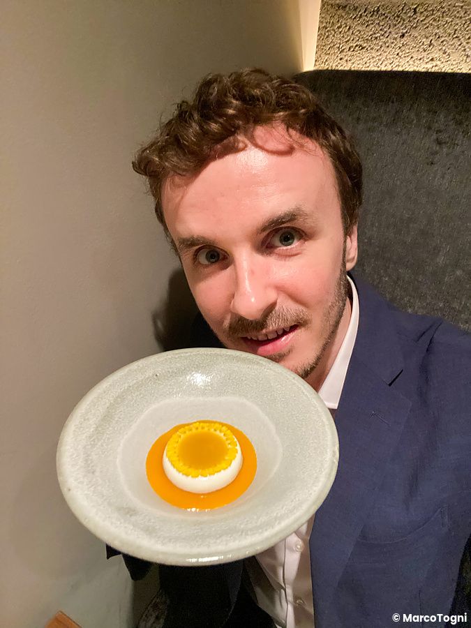 Marco Togni tiene in mano un dessert con crema bianca, coulis alla frutta e petali gialli al ristorante Crony, Tokyo.