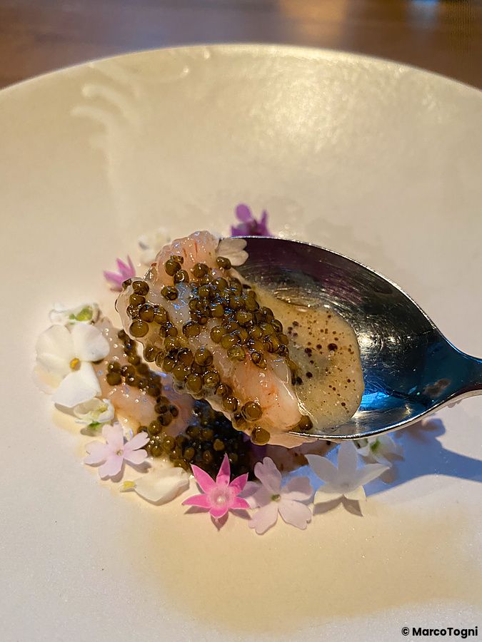 Un gambero con caviale di pomodoro su un cucchiaio d'argento, servito su un piatto decorato con fiori al Ristorante Crony,...