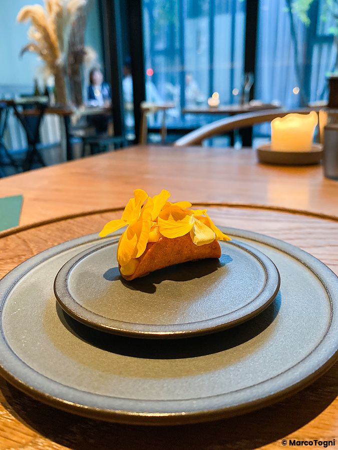 Mais e riccio di mare servito su un piatto circolare al Ristorante Crony, Tokyo, con fiori gialli a guarnizione.