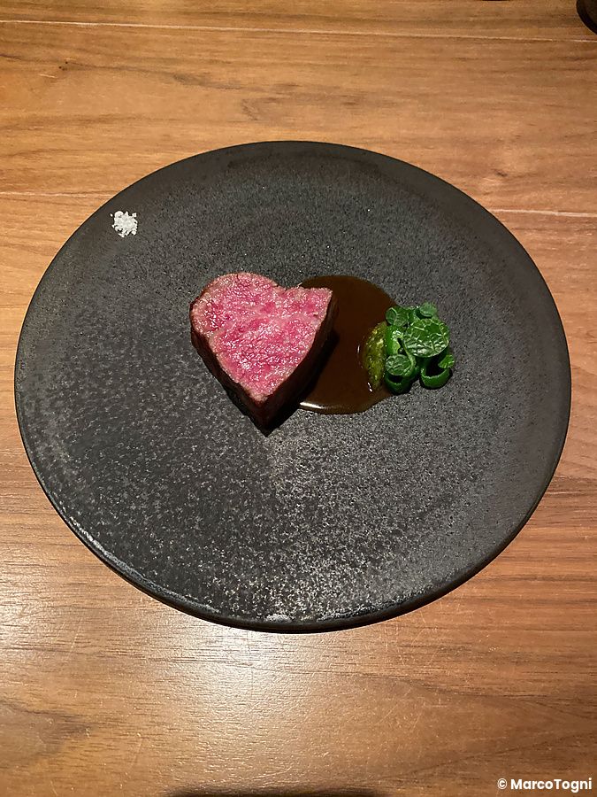 Carne di manzo tagliata a forma di cuore servita con salsa e verdure su un piatto scuro al Ristorante Crony, Tokyo.