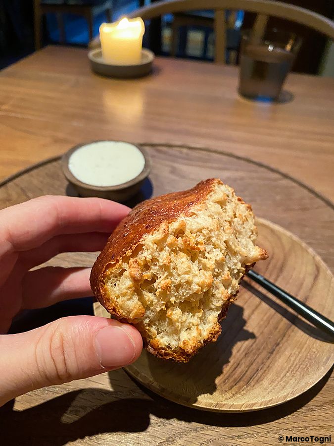 Pane artigianale tenuto in mano al ristorante Crony, Tokyo, con una ciotolina di crema su un piatto di legno.