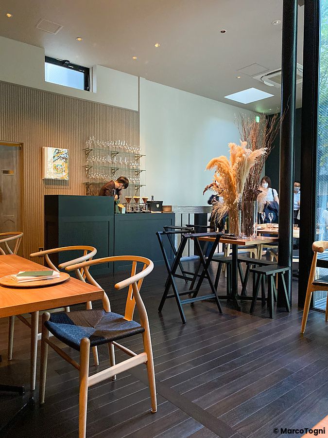 Interno del Ristorante Crony, Tokyo, con tavoli in legno, sedie moderne e una persona che lavora al banco bar.