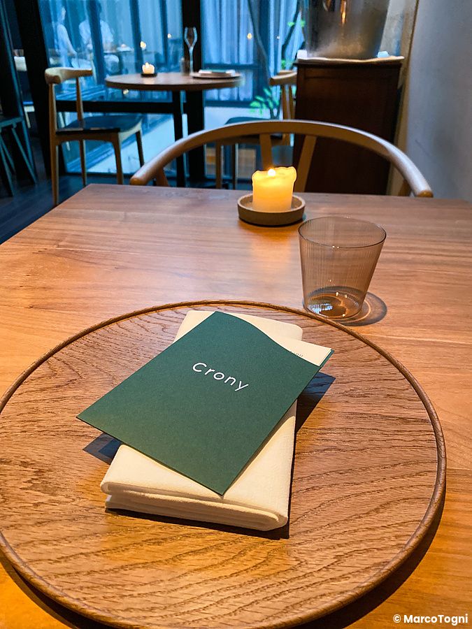Un tavolo in legno apparecchiato con menu, bicchiere e candela presso il Ristorante Crony, Tokyo.