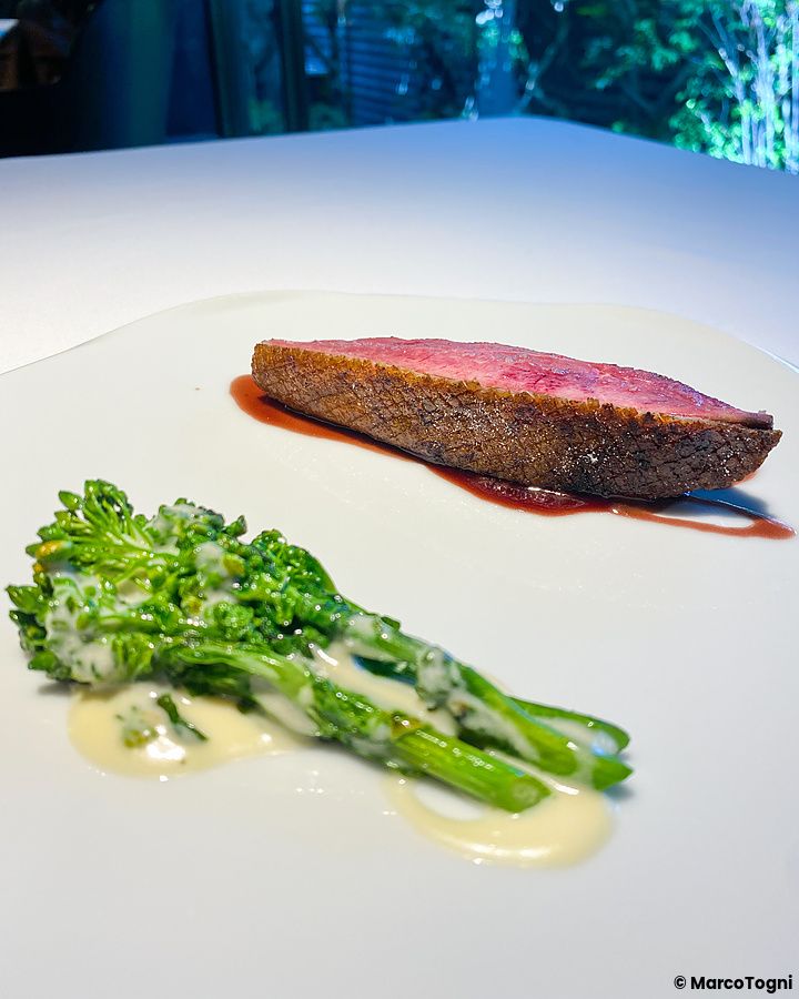 Carne d'anatra cotta al barbecue accompagnata da broccoletti su un piatto bianco a L'Effervescense, Tokyo.