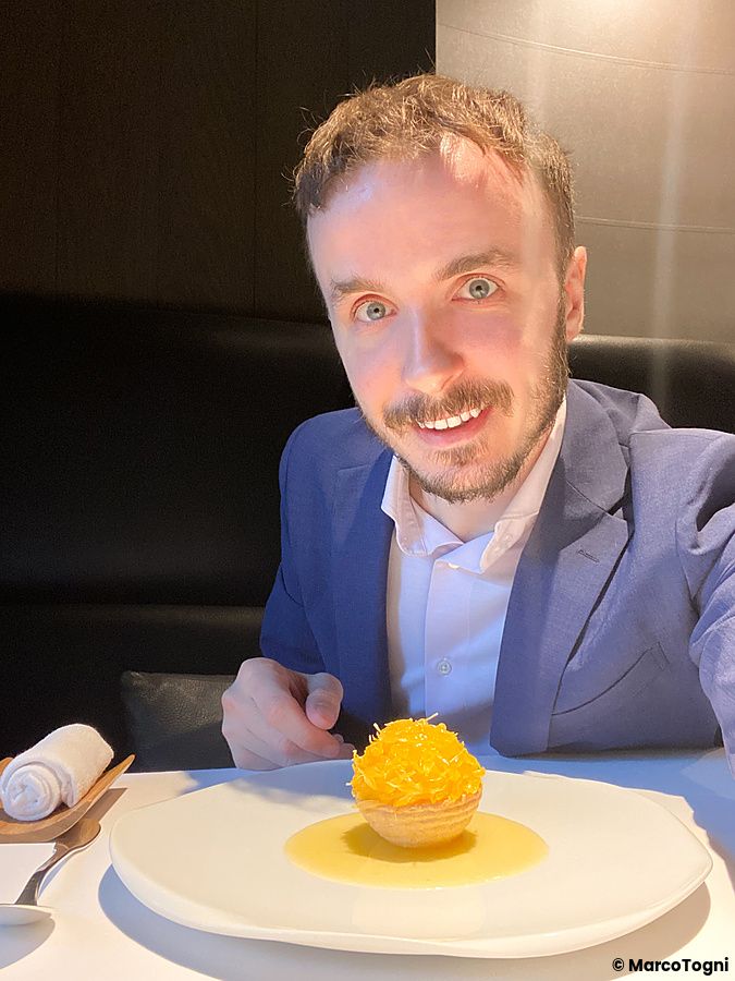 Marco Togni sorride seduto al tavolo davanti a un dolce con agrume hassaku, che viene ricomposto a L'Effervescense a Tokyo.