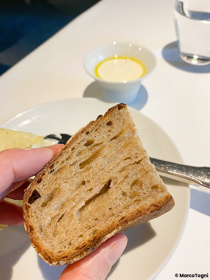 Una mano tiene una fetta di pane con crema vegana servita in una ciotolina presso il ristorante L'Effervescense a Tokyo.