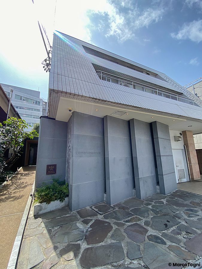 L'ingresso e la facciata esterna del ristorante L'Effervescense a Tokyo, caratterizzata da una moderna struttura in pietra.