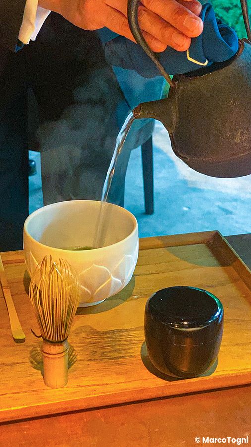 Preparazione del tè matcha servito nel ristorante L'Effervescense a Tokyo, con teiera in ghisa e ciotola in ceramica.