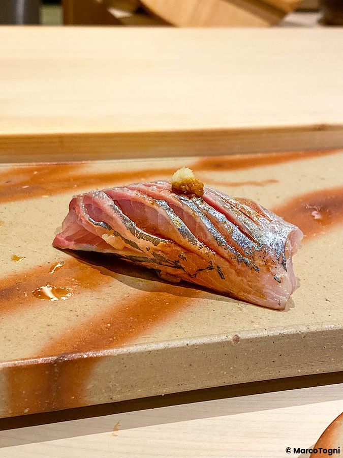 Un nigiri di aji con guarnizione servito su un piatto di ceramica decorato al Sushi Ginza Onodera Souhonten.