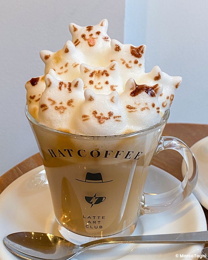 Tazza in vetro con logo Hatcoffee colma di schiuma di latte sagomata a forma di gattini presso Hatcoffee a Asakusa.